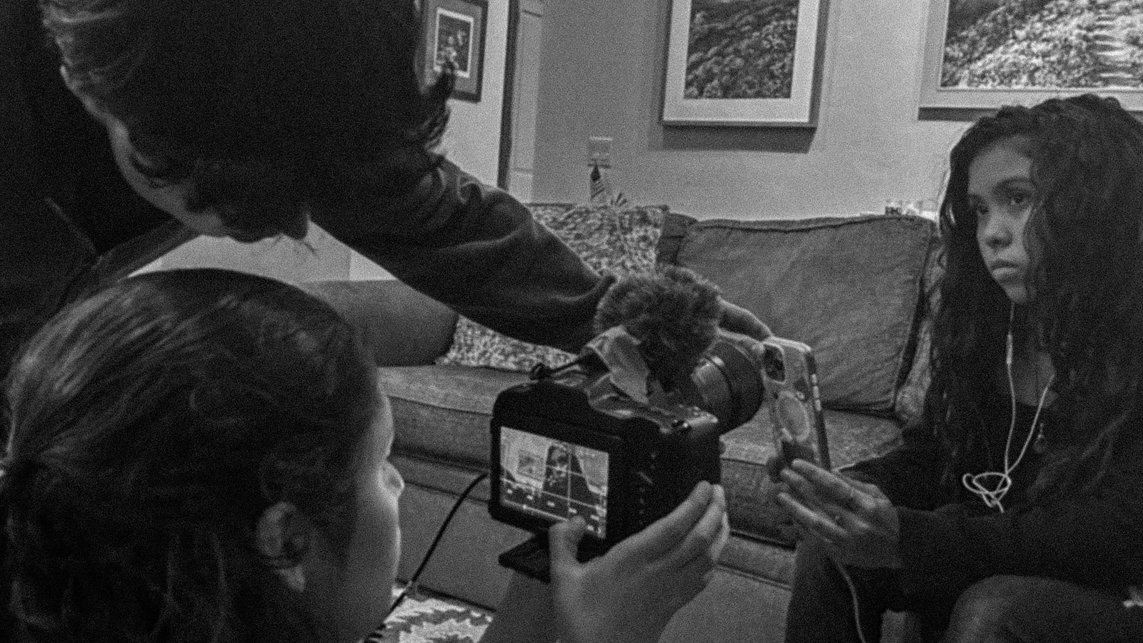 Two students operating a camera and boom microphone while filming an actor on a sofa